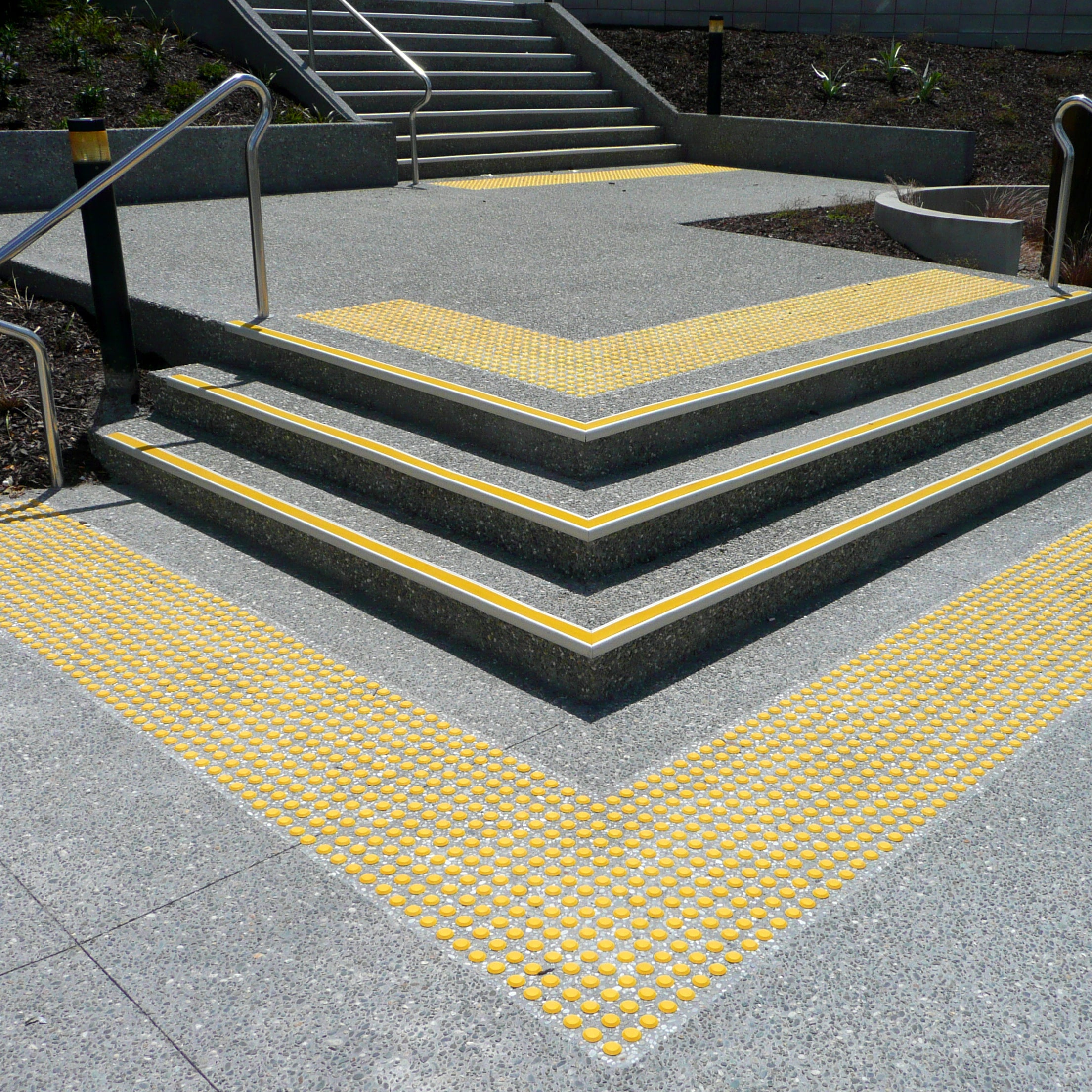 TacPro yellow polyurethane tactile indicator warning studs on honed exposed aggregate concrete at the tops and bottoms of stairs