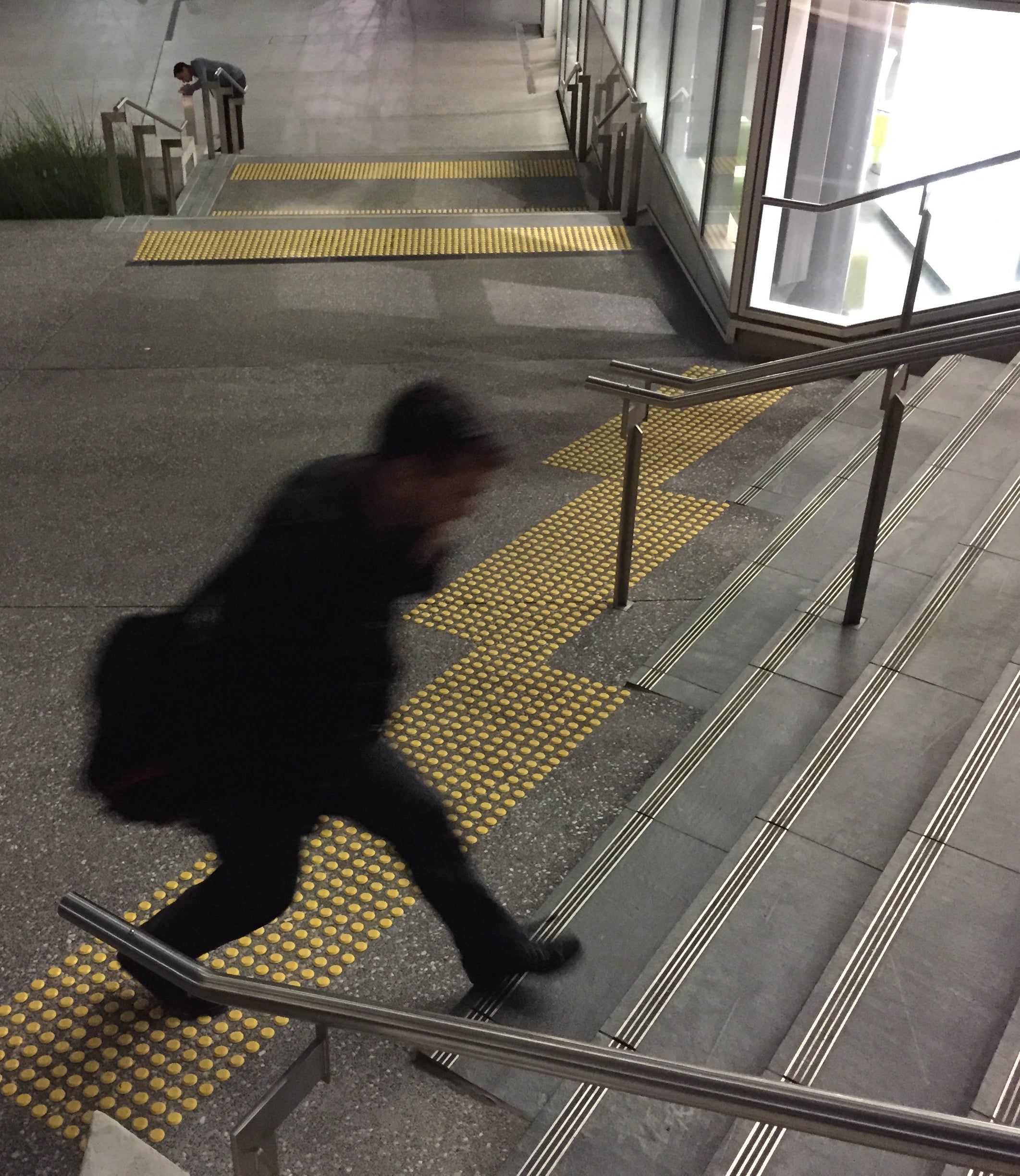 High angle of man using stairs. TacPro yellow polyurethane tactile indicator warning studs at top and bottom of stairs